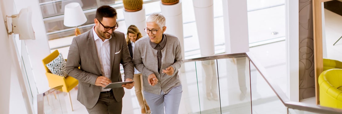 Business Feng Shui Bild von Arbeitskollegen, die eine Treppe in einem Bürogebäude hinaufgehen und sich unterhalten. Helle, moderne Umgebung. Mit Business Feng Shui ein noch produktiveres und angenehmeres Arbeitsumfeld schaffen.