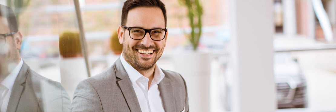 Business Coaching Bild von einem fröhlich lachenden Geschäftsmann, der direkt in die Kamera schaut. Helle, moderne Umgebung. Mit Coaching den Fokus des Einzelnen stärken.