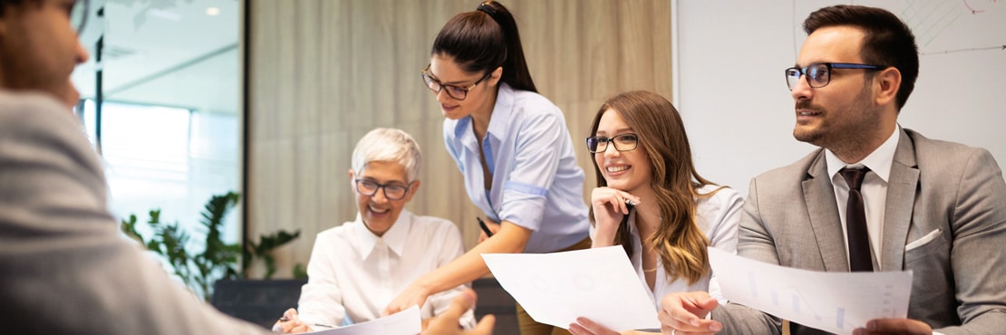 Projektmanagement Bild von fünf Arbeitskollegen, die in einem modernen Besprechungsraum gemeinsam den Projektstand diskutieren. Mit Projektmanagement und einer guten Moderation bessere Ergebnisse in der Zusammenarbeit erzielen.